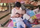 single mother breastfeeds her two children while selling vegetables.
